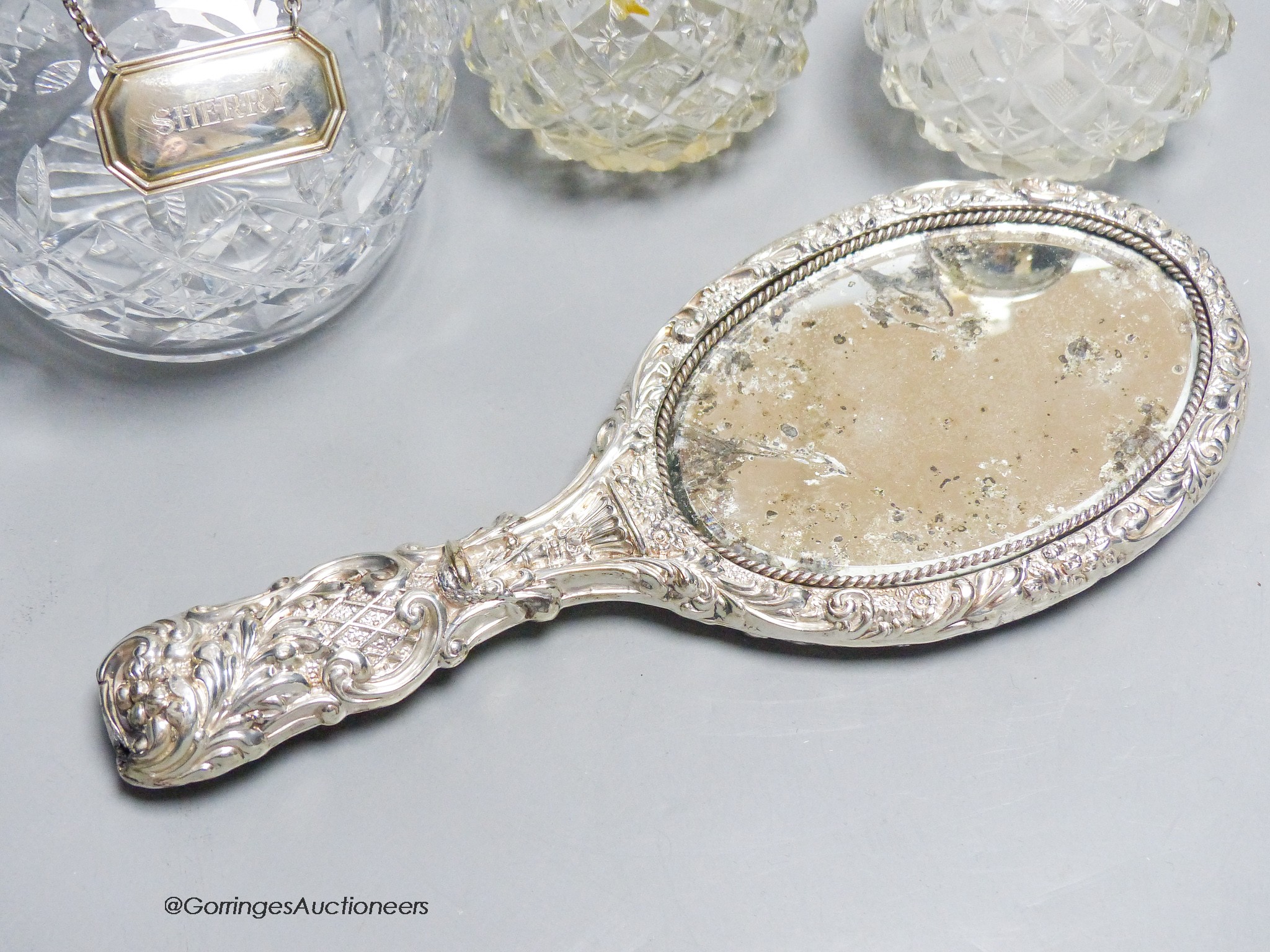 A pair of George V silver mounted scent bottles, (a.f.) 11.6cm, a repousse silver mounted hand mirror and a glass decanter with a silver wine label.